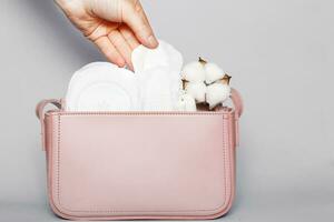 Women's hand takes out panty liner from pink cosmetic bag with tampons and feminine sanitary pads photo