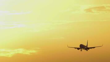 Airplane silhouette approaching landing in beautiful golden sunset. Background of cloudy fiery red sky. Concept travel video