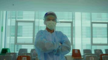 Porträt von ein Krankenschwester Mann mit gekreuzt Waffen tragen ein Gesicht Maske und Putten auf ein Gesicht Schild suchen beim das Kamera im ein Krankenhaus medizinisch Konzept. video