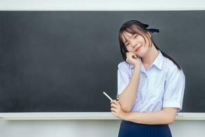 Cute Asian high school student girl in the school uniform with smiles confidently while she looks at the camera happily .in the classroom at school. photo