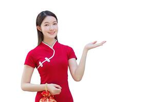 Young Asian beautiful confident woman in red dress stands holding red bag is pointing hand to present something while isolated on white background in Chinese new year theme. photo