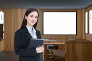 Asian professional business young woman in black suit smiles happily stand with confidence and look at the camera while she works and holds tablet in office. photo