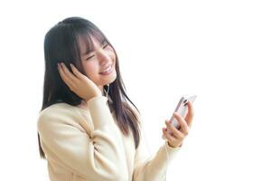 Young Asian student wearing long sleeves is sitting and smiling using her smartphone and headphones to listen to music while waiting for her to attend school while isolated on white background. photo