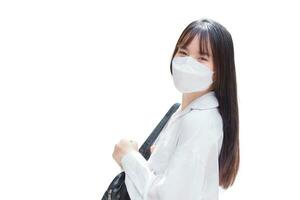 Confident young Asian female who wears a white shirt and bag while wearing a mask to prevent disease smiles happily and looks at the camera as she commute to work while isolated on white background photo