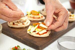 Adding toppings to the mini pizzas. Delicious homemade mini pizzas preparation. photo