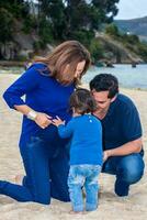 Young couple waiting for their second baby having fun with their baby girl at the beautiful white beach of Lake Tota located in the department of Boyaca at 3,015 meters above sea level in Colombia photo