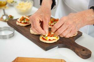 Adding toppings to the mini pizzas. Delicious homemade mini pizzas preparation. photo