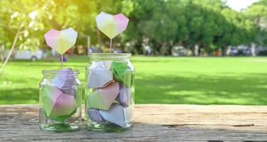 Paper hearts in glass bottles on wooden floor with blurred trees background concept for cheering LGBTQ people around the world photo