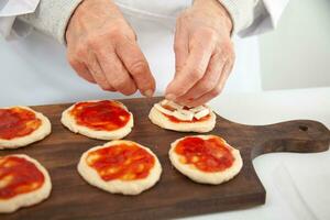 agregando coberturas a el mini pizzas agregando queso. delicioso hecho en casa mini pizzas preparación. foto