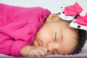 Closeup of a sweet little one month baby sleeping dressed in pink wearing a bow photo