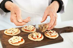 agregando coberturas a el mini pizzas agregando hongos. delicioso hecho en casa mini pizzas preparación. foto