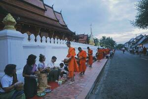 luang prabang Laos - 20 de julio de 2023 ,aldeano y turista ofrecimiento pegajoso arroz a budista monje en temprano Mañana a wat sensoukharam más famoso punto de referencia en luang prabang foto