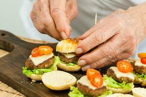 Putting on a toothpick on burger. Step by step preparation of mini burgers. Homemade mini burgers for children or appetizers. Small hamburgers. Assembling burgers photo