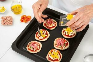 Adding toppings to the mini pizzas. Adding pineapple to the Hawaiian pizza. Delicious homemade mini pizzas preparation. photo