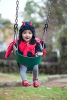Little baby girl wearing a ladybug costume sitting on a toddler Swing. Halloween concept. photo