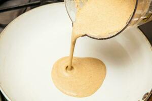 Quinoa crepes preparation. Pouring the quinoa crepes batter into a frying pan photo