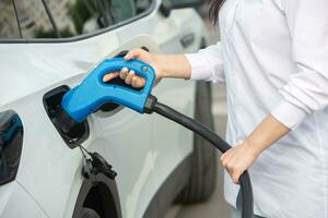 Young business woman refueling her electric car at a EV charging station. Concept of environmentally friendly vehicle. Electric car concept. Green travelling. photo