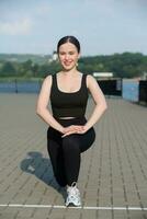 Young woman in black sportswear exercising outdoors. Fitness and healthy lifestyle concept. The white girl does sports in the park. photo