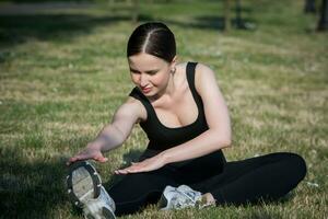 Young woman in black sportswear exercising outdoors. Fitness and healthy lifestyle concept. The white girl does sports in the park. photo