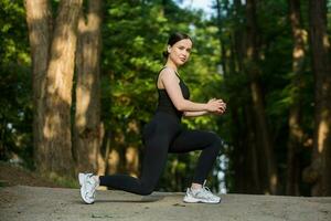 Young woman in black sportswear exercising outdoors. Fitness and healthy lifestyle concept. The white girl does sports in the park. photo