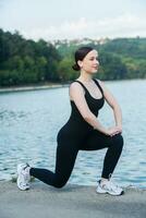 joven mujer en negro ropa de deporte hacer ejercicio al aire libre. aptitud y sano estilo de vida concepto. el blanco niña lo hace Deportes en el parque. foto