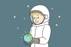 Boy dressed as astronaut is holding miniature planet earth, located in space with starry sky photo