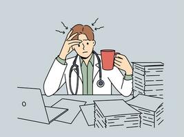 Frustrated doctor with cup of coffee sits at table with pile of papers and needs help of assistant photo