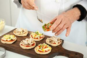 agregando coberturas a el mini pizzas agregando vegetales. delicioso hecho en casa mini pizzas preparación. foto