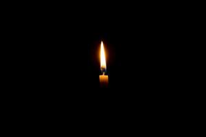 soltero ardiente vela fuego o ligero brillante en un pequeño blanco vela en negro o oscuro antecedentes en mesa en Iglesia para Navidad, funeral o monumento Servicio con Copiar espacio. foto