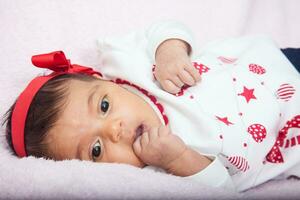 de cerca de un dulce uno mes bebé niña con un sorpresa expresión vistiendo un rojo y blanco t camisa. foto