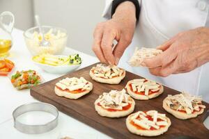 Adding toppings to the mini pizzas. Adding chicken. Delicious homemade mini pizzas preparation. photo