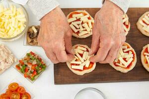 Adding toppings to the mini pizzas. Adding cheese. Delicious homemade mini pizzas preparation. photo