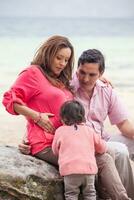 Young couple waiting for their second baby having fun with their baby girl at the beautiful white beach of Lake Tota located in the department of Boyaca at 3,015 meters above sea level in Colombia photo