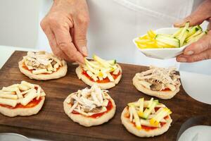 Adding toppings to the mini pizzas. Adding vegetables. Delicious homemade mini pizzas preparation. photo