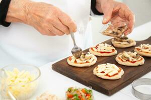 agregando coberturas a el mini pizzas agregando hongos. delicioso hecho en casa mini pizzas preparación. foto