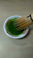 Matcha green tea in a bowl with bamboo whisk, close up photo