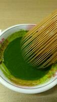 Matcha green tea in a bowl with bamboo whisk, close up photo