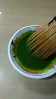 Matcha green tea in a bowl with bamboo whisk, close up photo