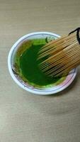 Matcha green tea in a bowl with bamboo whisk, close up photo