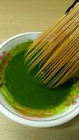 Matcha green tea in a bowl with bamboo whisk, close up photo