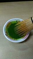 Matcha green tea in a bowl with bamboo whisk, close up photo