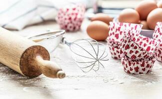 Baking utensils with eggs flour and cupcake cases on kitchen table - Close up photo