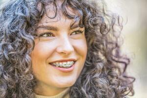 Portrait of a happy smiling young woman with dental braces and and curly hair photo