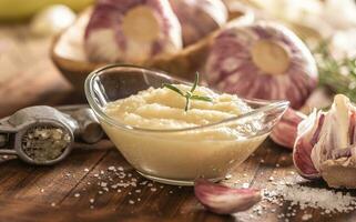 Garlic paste in a glass bowl with peeled garlic, salt and garlic heads photo