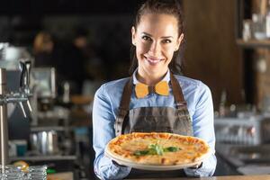 camarera sonrisas mientras servicio grande auténtico italiano Pizza en un restaurante foto