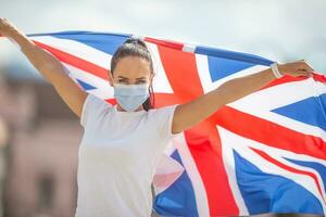 joven mujer en un protector máscara sostiene Reino Unido bandera durante pandemia foto