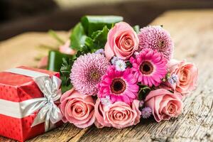 Beautiful bouquet of flowers with red gift on wooden table. photo
