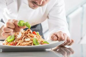 Chef in restaurant kitchen prepares and decorates meal with hands.Cook preparing spaghetti bolognese photo