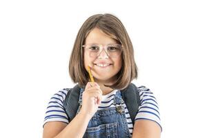 Smiling cute young schoolgirl in glasses holds pencil close to her mouth photo