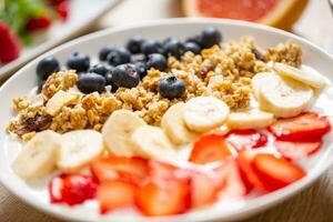 sano desayuno servido con plato de yogur muesli arándanos fresas y banana. foto